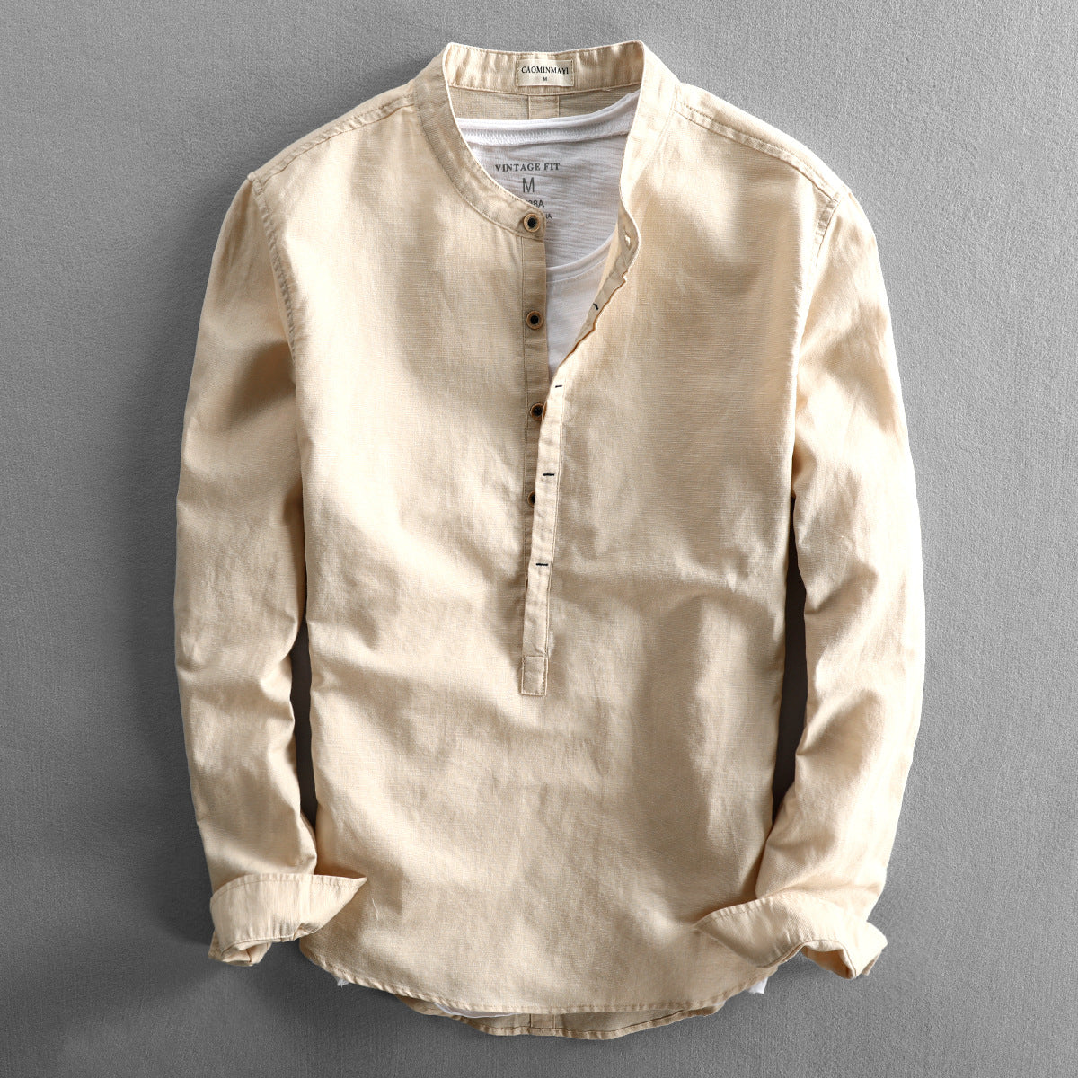 Beiges Herrenhemd mit Stehkragen, Knopfleiste und langen Ärmeln auf grauem Hintergrund. Modisches, lässiges Design für stilvolle Outfits.