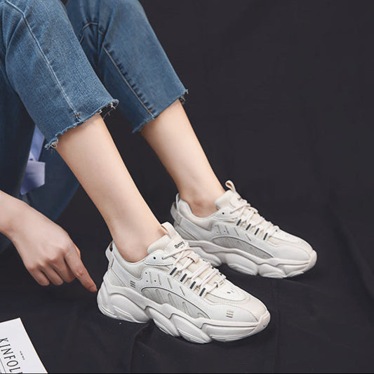 Weiße Chunky Sneaker an den Füßen einer Person in blauen Jeans auf schwarzem Hintergrund. Modische Sportschuhe, lässiger Stil, Trend 2023.