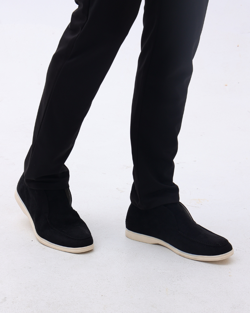 Schwarze Herren-Sneaker aus Wildleder mit weißer Sohle, getragen zu eleganten schwarzen Hosen auf weißem Hintergrund. Modische Herrenschuhe.