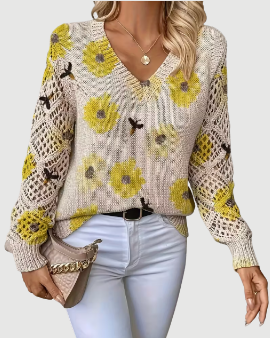 Frau trägt beige Strickpullover mit gelben Blumenmuster, kombiniert mit weißer Hose und beiger Handtasche. Modetrend, Herbstmode, Damenbekleidung.