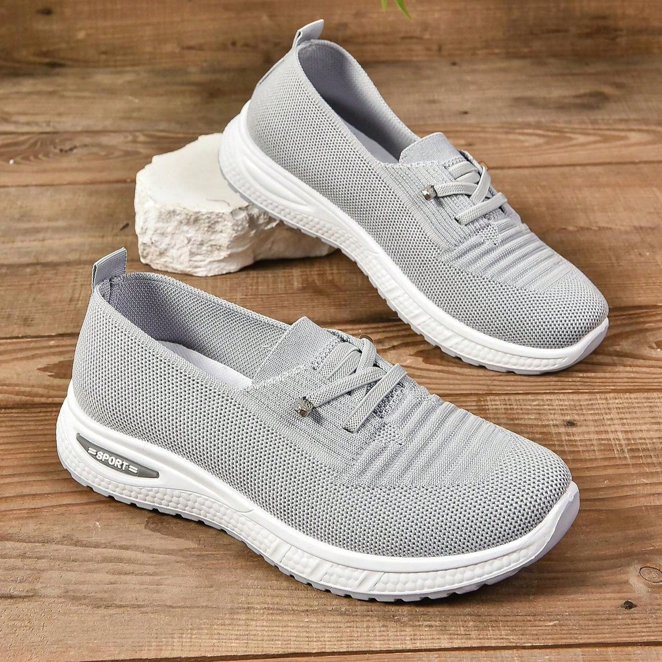 Graue Damen-Sneaker auf Holzboden, atmungsaktives Mesh-Design, weiße Sohle, sportlich, bequem, ideal für Freizeit und Sport.