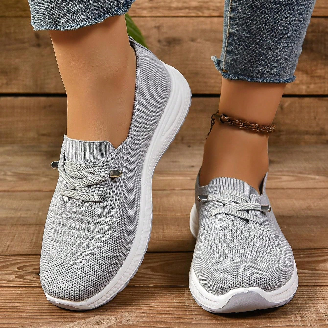 Graue Damen-Sneaker aus Strickmaterial, getragen mit blauen Jeans, auf Holzboden. Bequeme, modische Freizeitschuhe für Alltag und Sport.