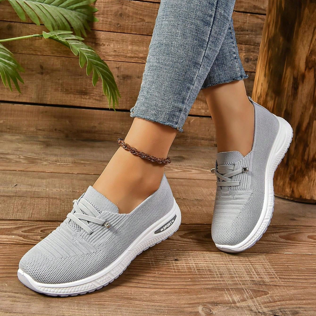 Graue Damen-Sneaker aus Strickmaterial, kombiniert mit blauen Jeans, auf Holzboden. Bequeme, modische Schuhe für Freizeit und Alltag.