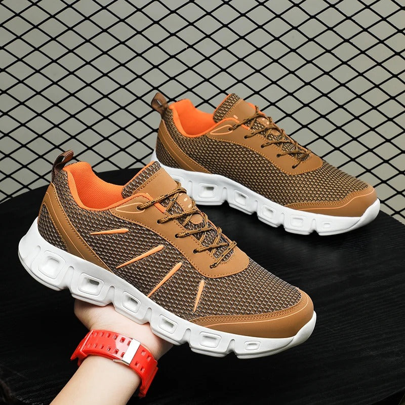 Braune Sportschuhe mit weißer Sohle, atmungsaktivem Mesh-Obermaterial und orangefarbenem Innenfutter, präsentiert vor einem Gitterhintergrund.