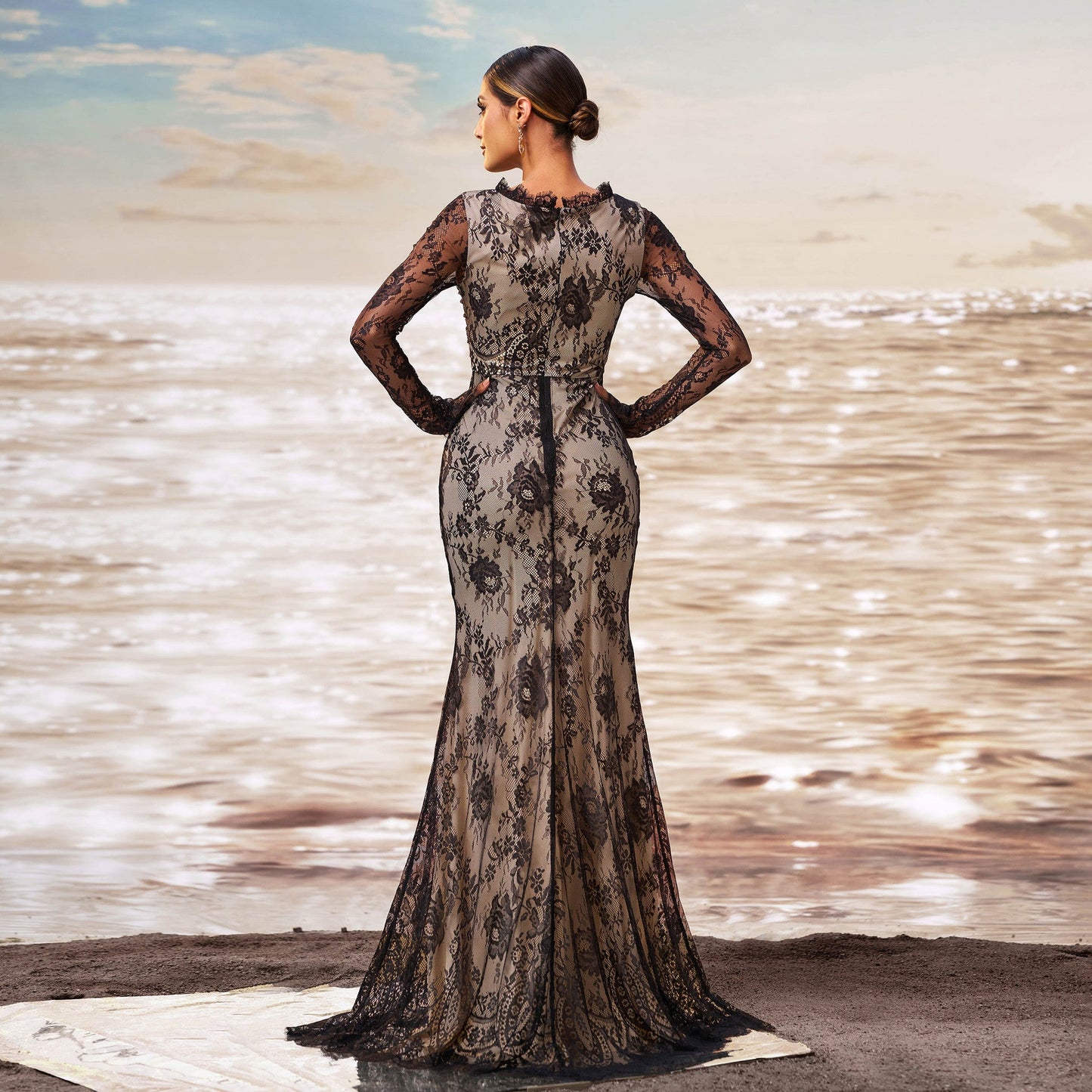 Frau in eleganter, bodenlanger Spitzenkleid am Strand, Sonnenuntergang im Hintergrund, stilvolle Abendmode, Meerblick, glamouröses Design.