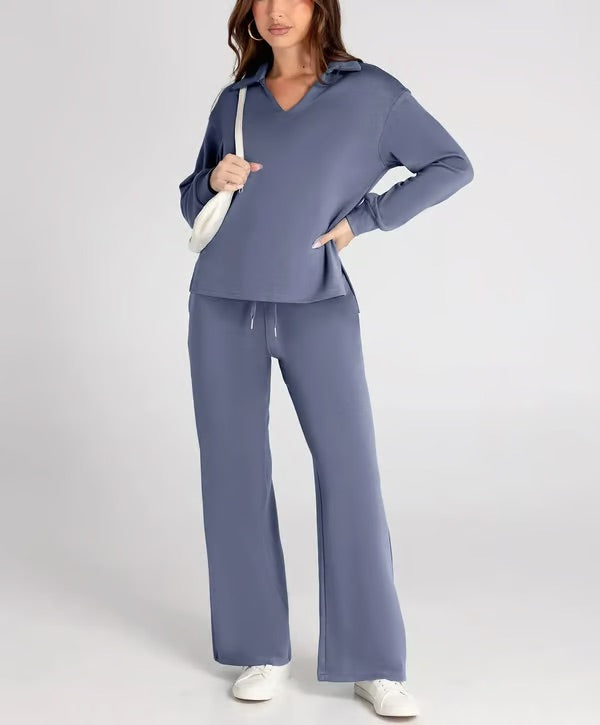 Frau in blauer Lounge-Wear, bestehend aus Pullover und Hose, mit weißer Tasche und Sneakers. Bequeme Damenmode, Freizeitoutfit, stilvoll und modern.