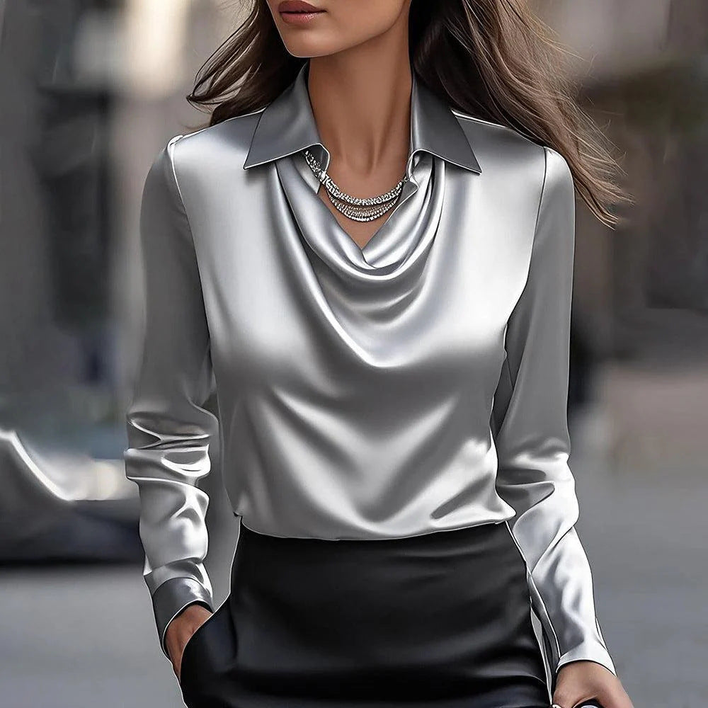 Frau in eleganter, silberner Satinbluse mit Kettenhalskette, modisch gekleidet, urbaner Hintergrund. Hochwertige Damenmode, stilvoller Look.