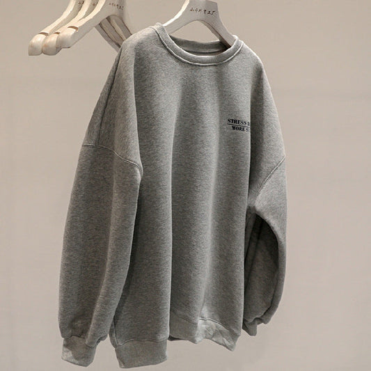 Grauer Oversize-Pullover mit Rundhalsausschnitt, minimalistischem Design und kleinem Schriftzug, hängend auf Holzkleiderbügeln.