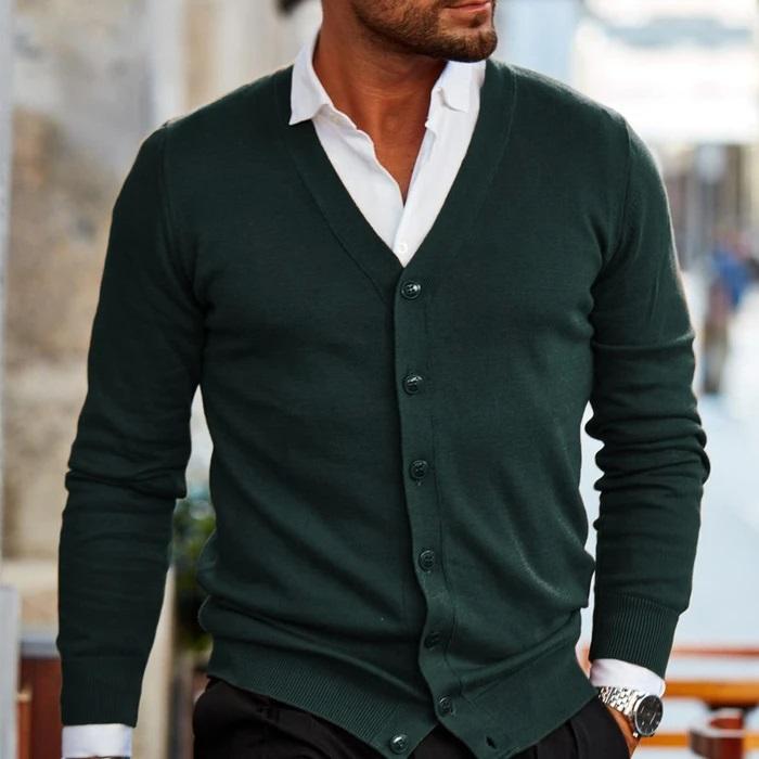 Mann in grünem Cardigan und weißem Hemd, stilvolle Herrenmode, elegantes Outfit, urbane Kulisse, modischer Look, Freizeitkleidung.