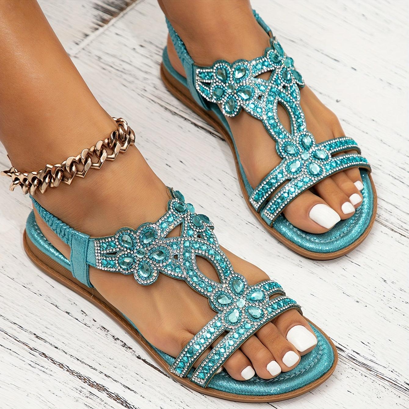 Türkise Sandalen mit Strasssteinen und Blumenmuster auf weißem Holzboden, getragen von einer Person mit Fußkettchen. Perfekt für Sommermode.