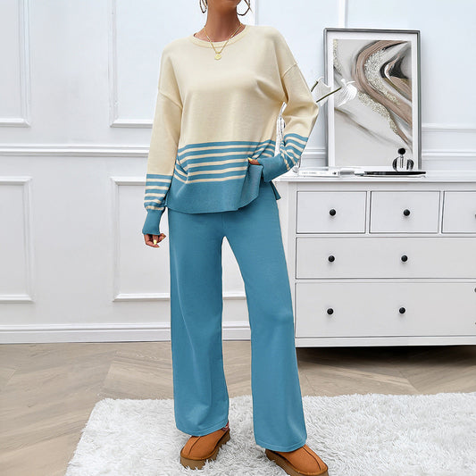 Frau in blau-beigem Strickset mit Streifen, steht in modernem Wohnzimmer. Modetrend, gemütlicher Look, stilvolle Damenbekleidung.