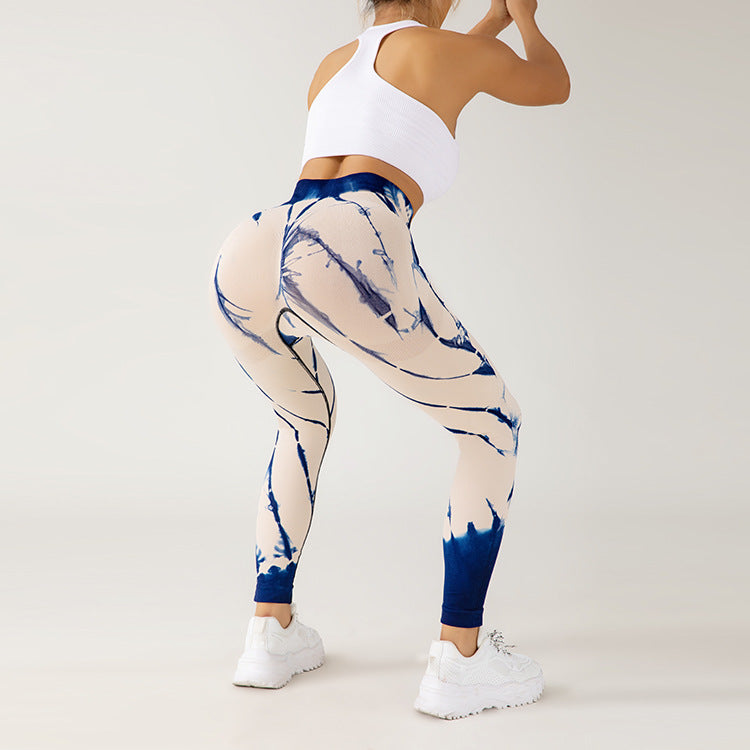 Frau in weißem Sport-BH und blau-weiß gemusterten Leggings beim Training, zeigt Fitnessmode, Sportbekleidung, aktive Lebensweise.