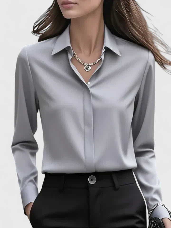 Frau in eleganter grauer Bluse und schwarzer Hose, trägt eine silberne Halskette. Businessmode, stilvolle Damenbekleidung, Bürooutfit.