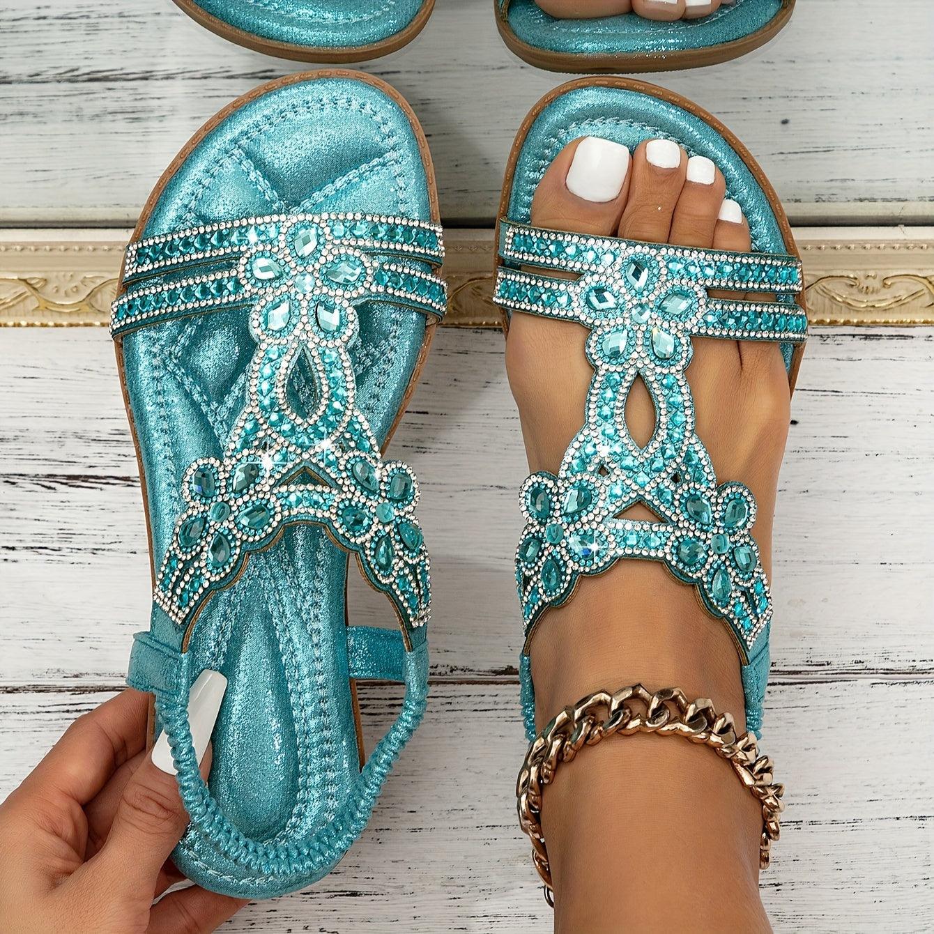 Türkise Sandalen mit Strasssteinen, verziertem Blumenmuster und gepolsterter Sohle auf weißem Holzboden. Elegante Sommerschuhe für Damen.