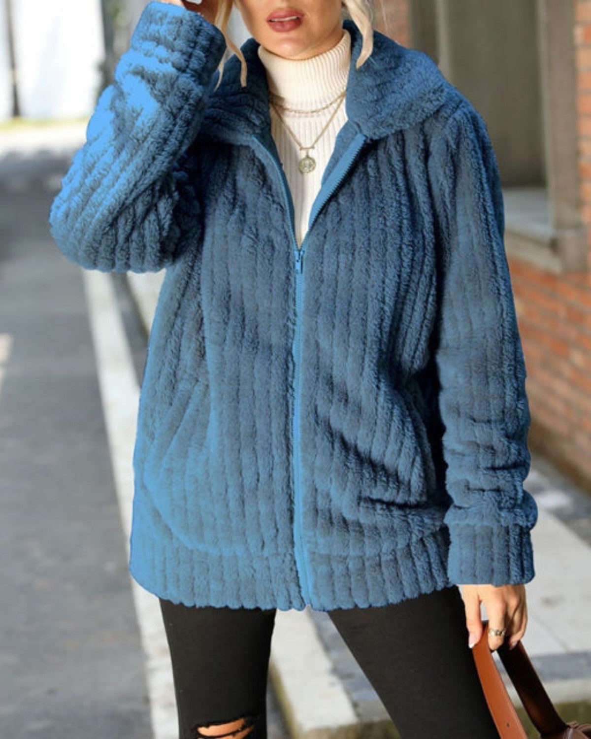 Frau in blauer Plüschjacke, weißem Rollkragenpullover und schwarzen Jeans auf Straße. Modetrend, Herbstmode, bequeme Damenbekleidung.