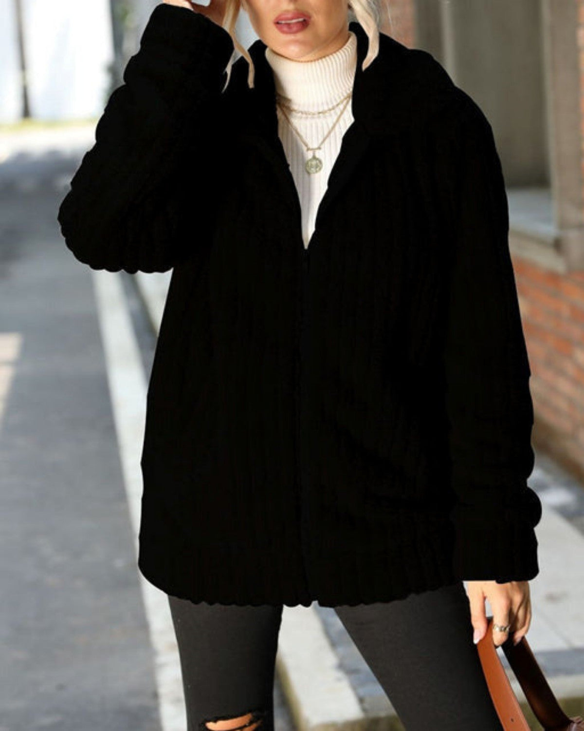 Schwarze Strickjacke Damenmode, kombiniert mit weißem Rollkragenpullover und grauer Hose, stilvoller Herbst-Look auf städtischer Straße.