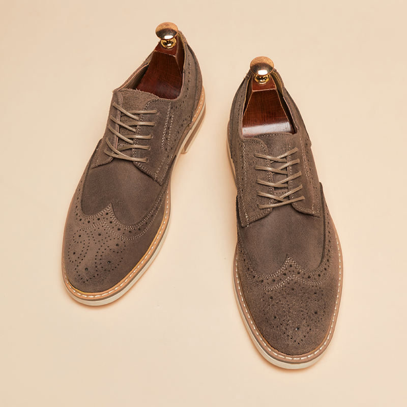 Braune Wildleder-Brogues mit Lochmuster und Holzschuhspanner auf beigem Hintergrund. Elegante Herrenschuhe, stilvoll und klassisch.