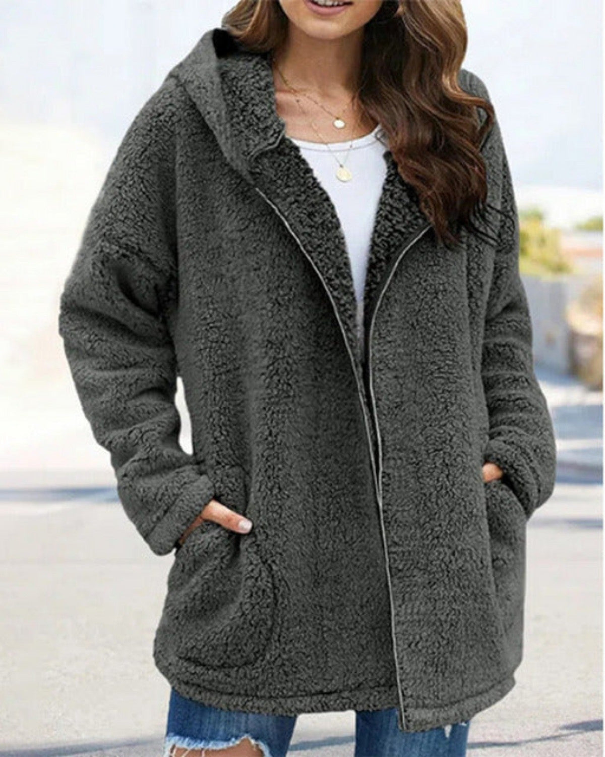 Frau in grauem Teddyfell-Mantel mit Kapuze, weißem Shirt und zerrissenen Jeans. Modetrend, Winterjacke, gemütlicher Look, Outdoor-Bekleidung.