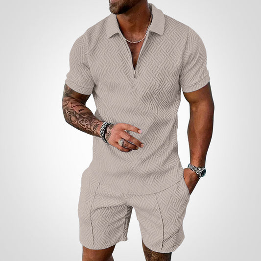 Mann in beigem, strukturiertem Kurzarm-Poloshirt und Shorts, tätowierter Arm, silberne Uhr und Kette, modischer Sommerlook.