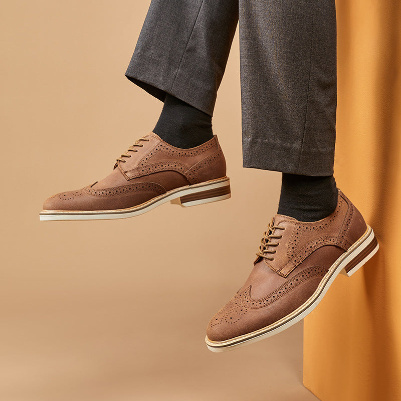 Braune Brogue-Schuhe aus Leder, getragen mit grauen Anzughosen und schwarzen Socken, vor beigem Hintergrund. Elegante Herrenschuhe, Business-Look.