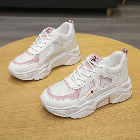 Weiße Damen-Sneaker mit rosa Akzenten und Herzmotiv auf Holztisch. Modische Turnschuhe, sportlich und trendy, ideal für Freizeit und Alltag.