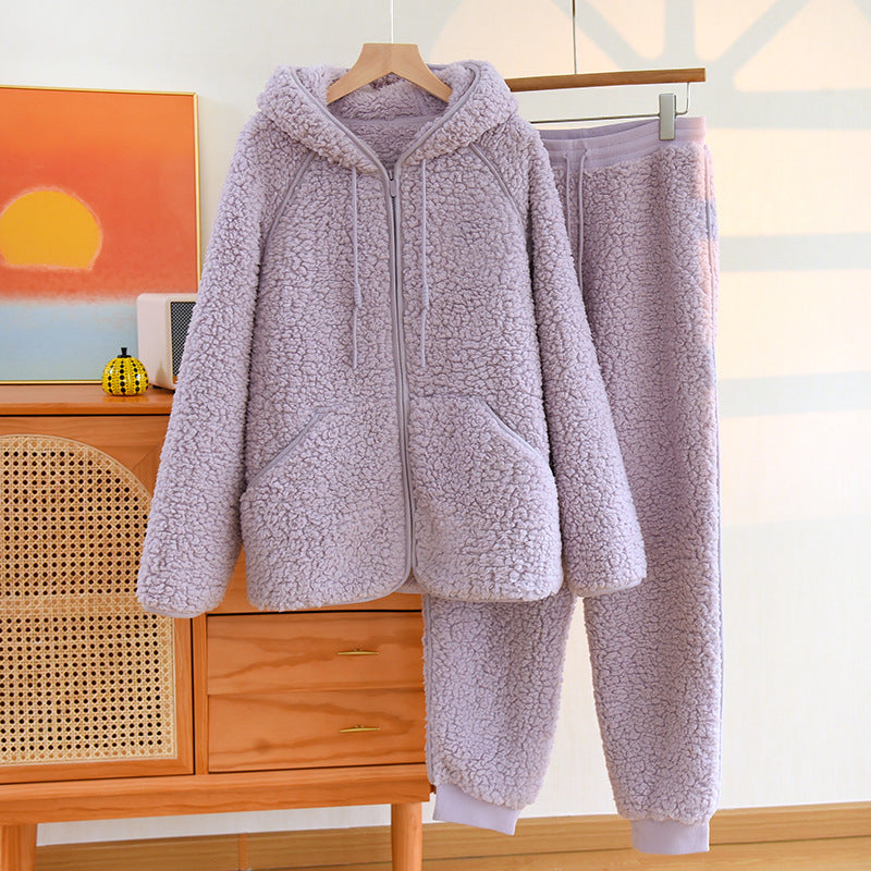 Fliederfarbener Fleece-Trainingsanzug mit Kapuze und Reißverschluss, hängend auf einem Kleiderbügel, im modernen Schlafzimmer mit Sonnenuntergangsbild.