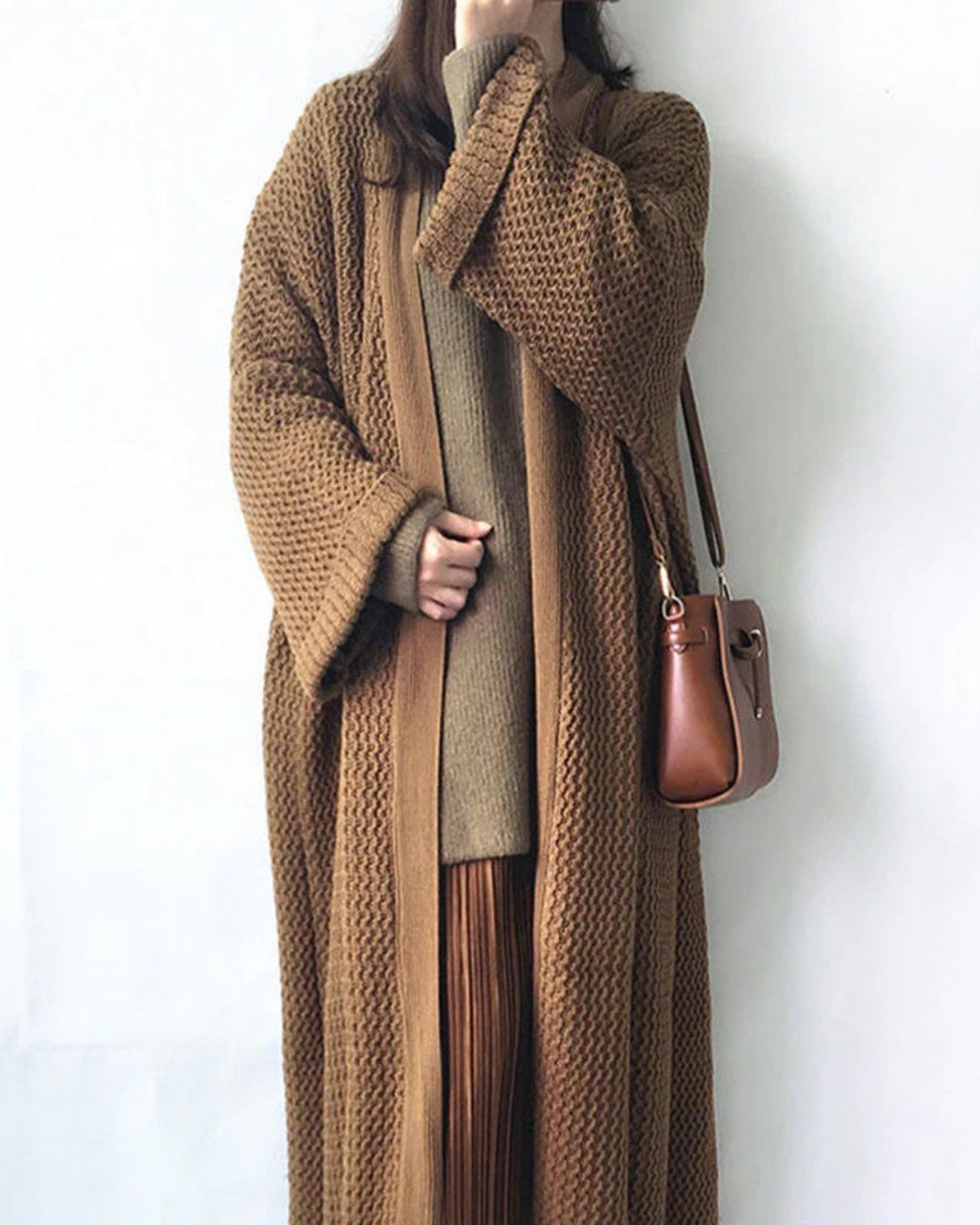 Frau in langem, braunem Strickmantel mit passender Tasche. Modetrend Herbst/Winter, gemütlicher Look, stilvolle Damenbekleidung.