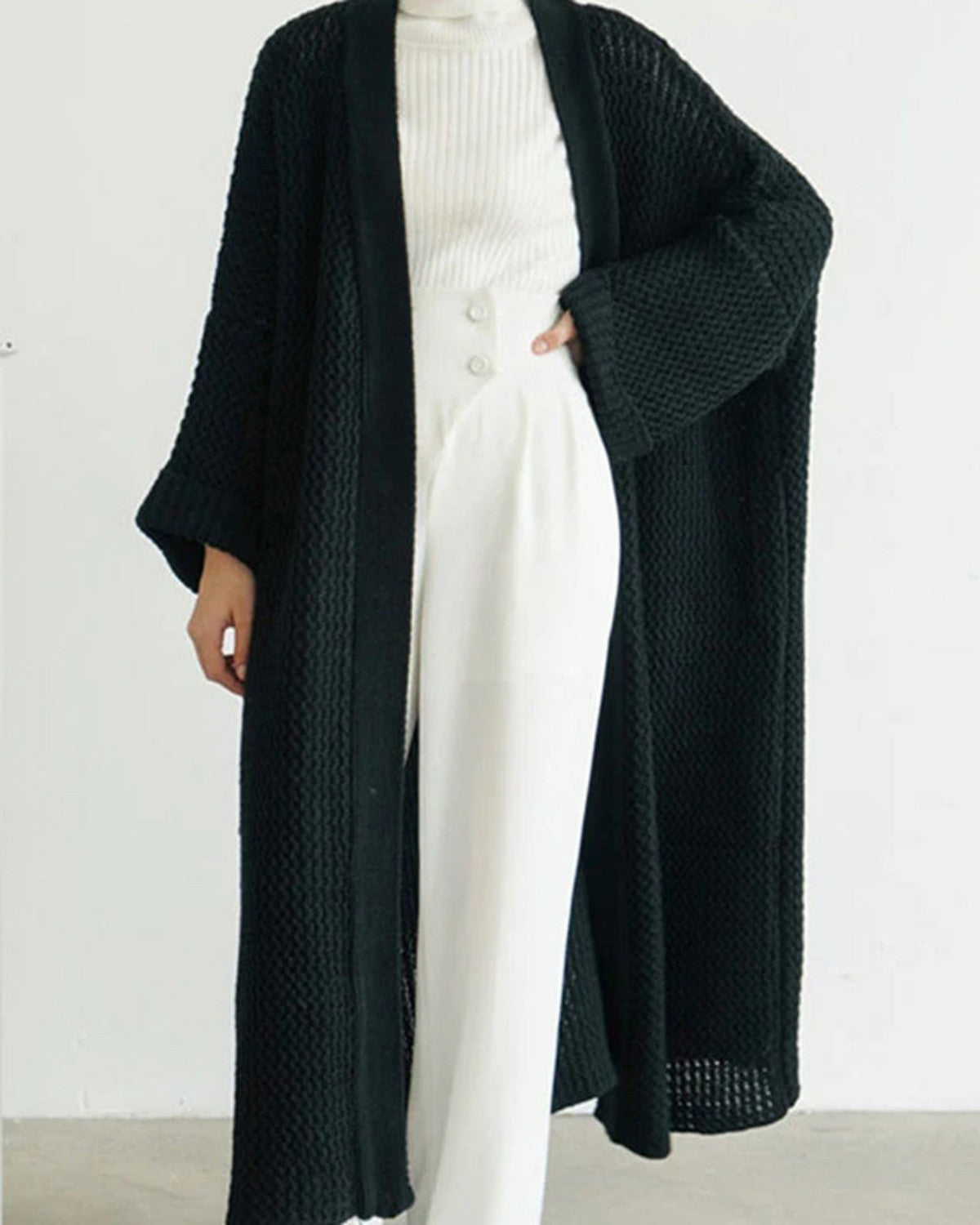 Schwarzer Strick-Cardigan, lang und offen, über weißem Rollkragenpullover und Hose. Modischer Damen-Look, ideal für Herbst und Winter.
