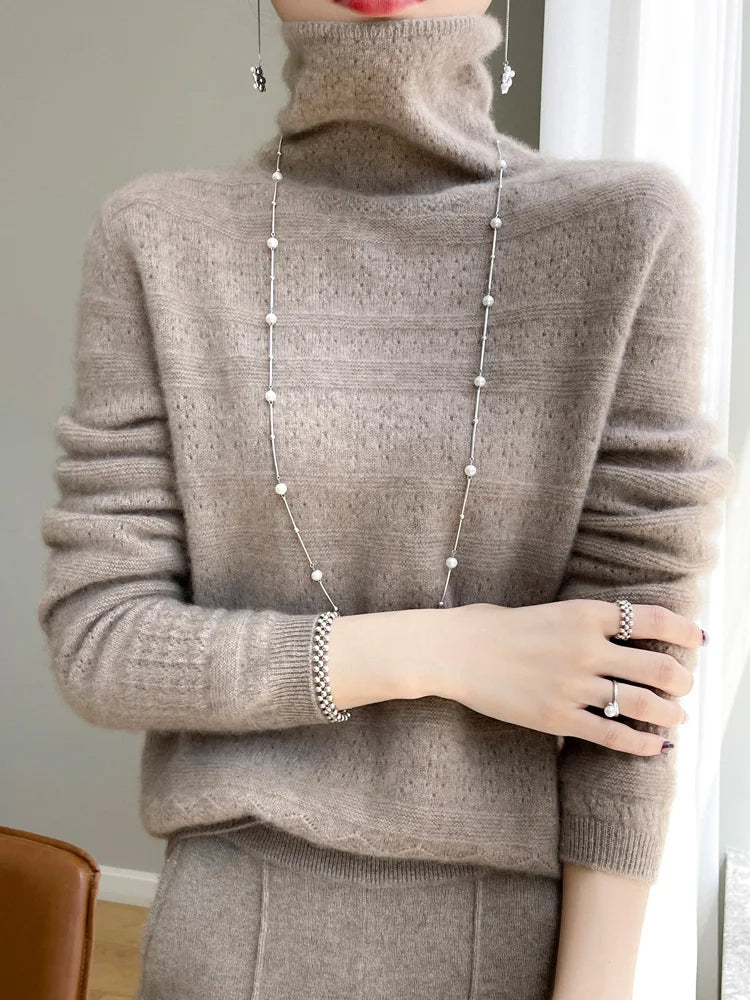 Frau in beigem Kaschmirpullover mit Rollkragen, trägt lange silberne Halskette und Ringe. Elegante Wintermode, luxuriöser Strick, Schmuck.