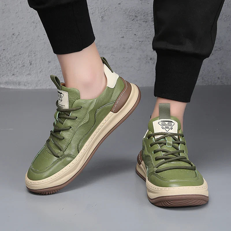 Grüne Sneaker mit brauner Sohle, getragen von Person in schwarzer Hose. Modische Turnschuhe, urbaner Stil, bequeme Freizeitschuhe.