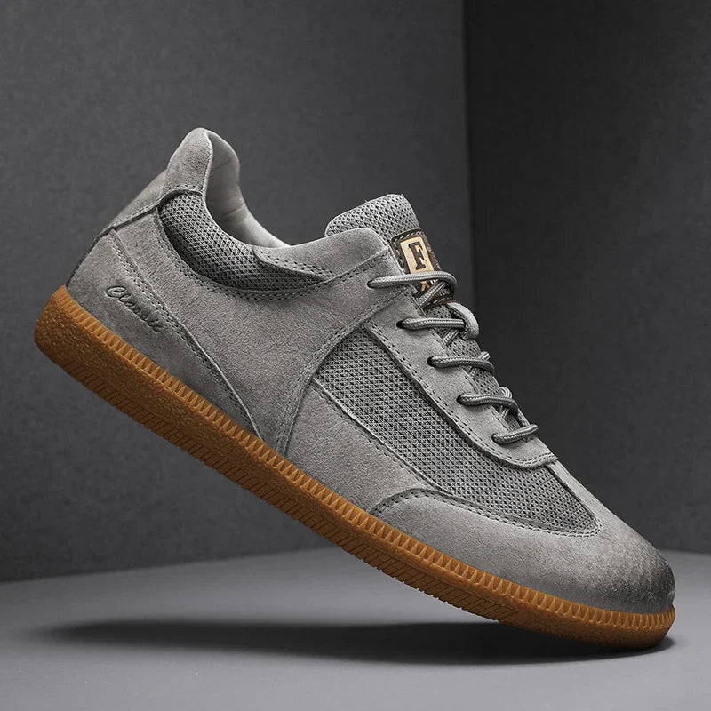 Grauer Sneaker mit brauner Sohle, seitlichem Logo und Mesh-Einsätzen, stilvoll und modern, ideal für Herrenmode und Freizeitkleidung.