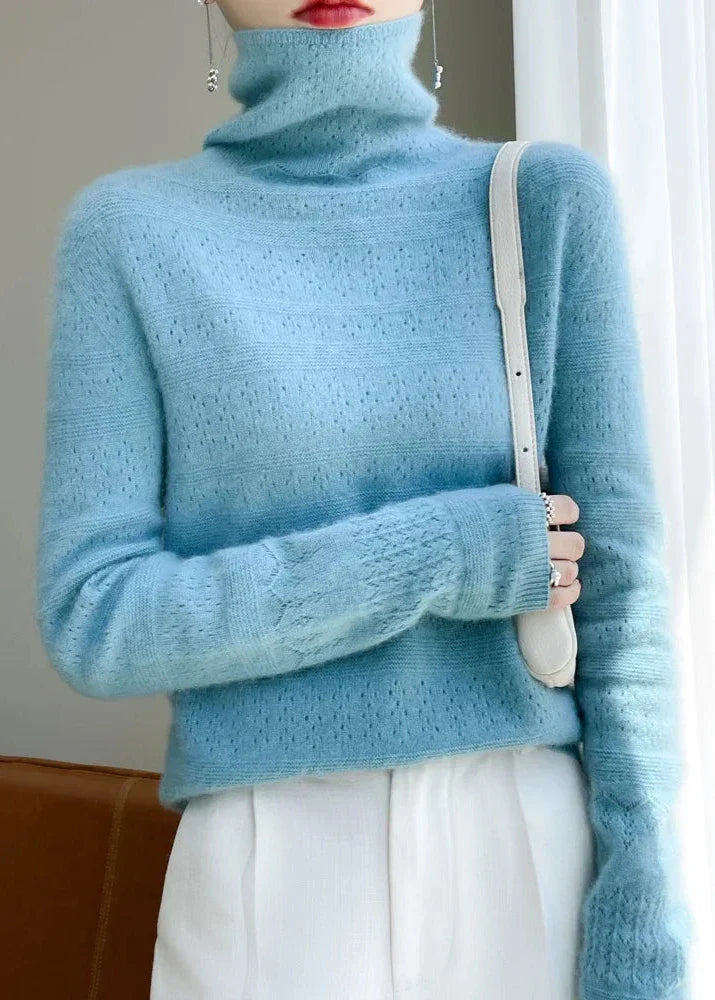 Frau in hellblauem Rollkragenpullover und weißer Hose, hält weiße Handtasche. Modetrend, Strickmode, eleganter Winterlook.