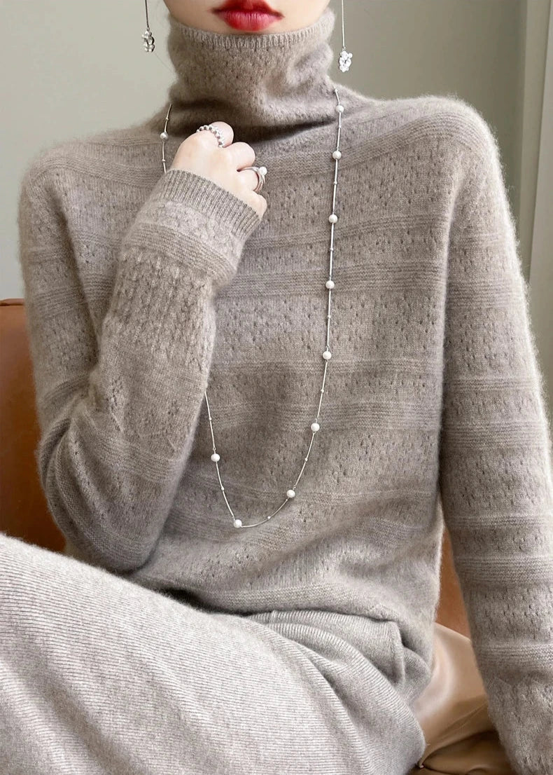 Frau in beigem Kaschmirpullover mit Rollkragen, trägt lange Perlenkette und roten Lippenstift. Elegante Wintermode, luxuriöser Strick.