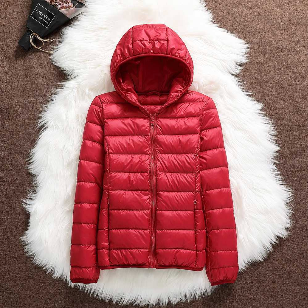 Rote Daunenjacke mit Kapuze auf weißem Fellteppich, modische Winterbekleidung, warme Outdoor-Jacke, stilvoll und funktional.