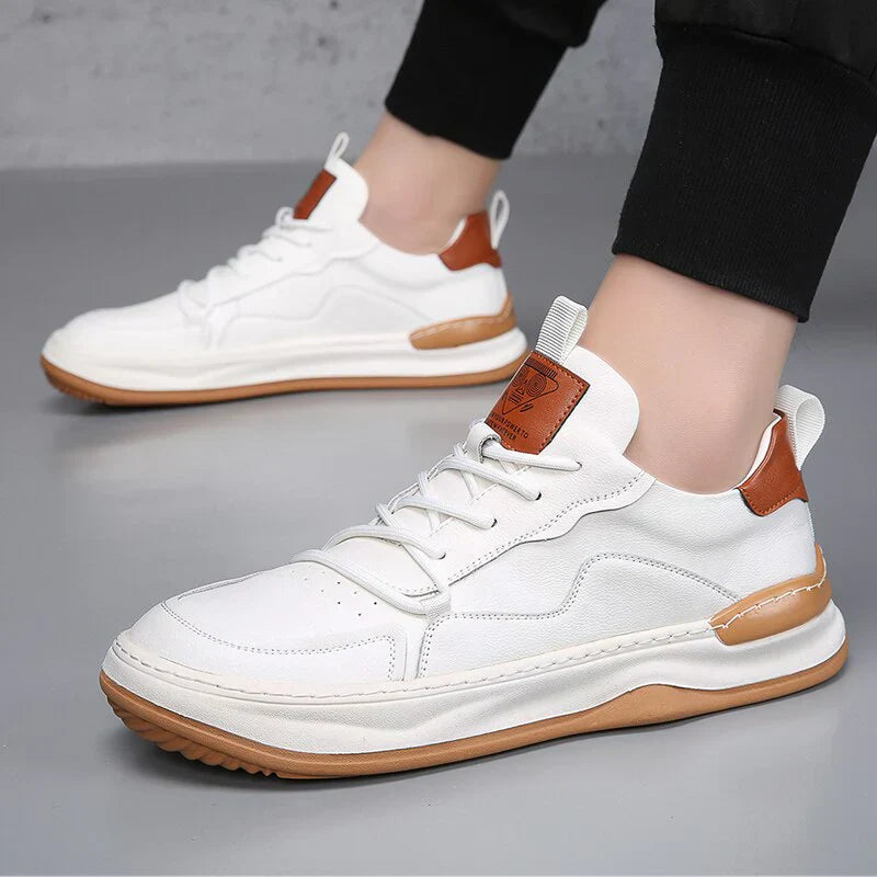 Weiße Sneaker mit braunen Akzenten, Gummisohle und Schnürsenkeln auf grauem Hintergrund. Modische Herrenschuhe, ideal für Freizeit und Sport.