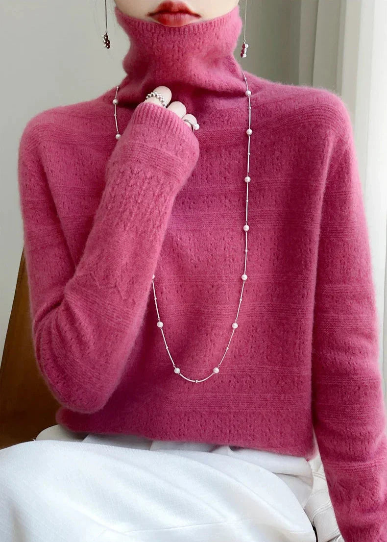 Dame in pinkem Rollkragenpullover mit langer Perlenkette, sitzt auf einem Stuhl. Elegante Wintermode, stilvoller Strickpullover, modisches Accessoire.