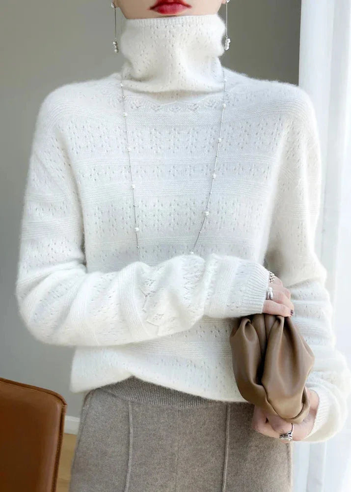 Frau in weißem Strickpullover mit Rollkragen, hält braune Clutch. Elegante Wintermode, stilvoller Look, modische Accessoires.