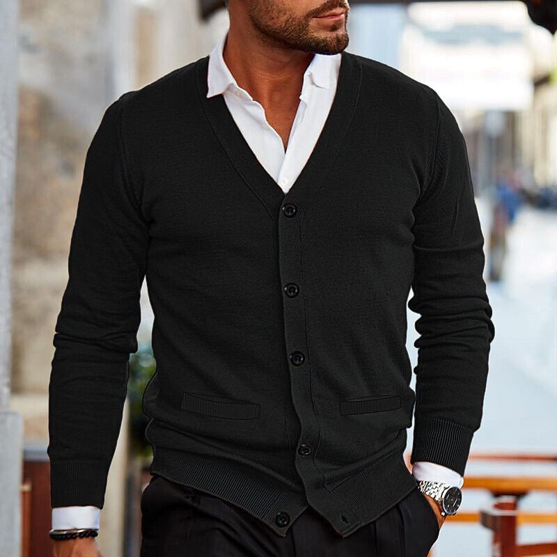 Mann in schwarzem Cardigan und weißem Hemd, stilvoll gekleidet, geht auf einer städtischen Straße. Elegante Herrenmode, Freizeitlook.