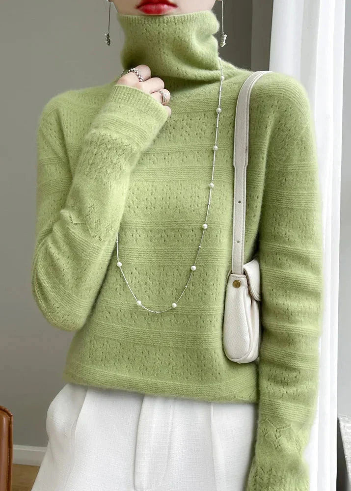 Frau in grünem Rollkragenpullover, weißer Hose und mit weißer Umhängetasche. Elegante Mode, Herbstoutfit, Damenbekleidung, stilvoller Look.