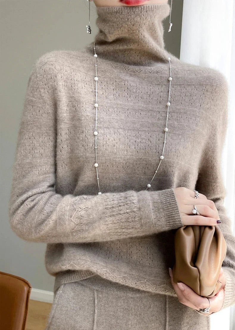 Frau in beigem Rollkragenpullover mit langer Halskette, hält braune Clutch. Elegante Wintermode, Strickpullover, Accessoires.