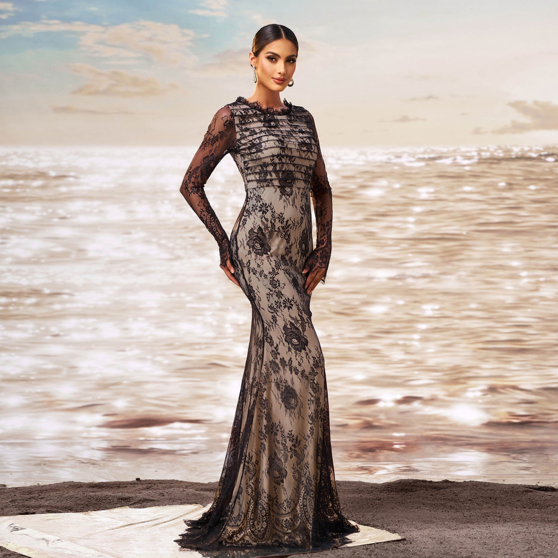 Elegantes Abendkleid mit schwarzer Spitze und floralen Mustern, getragen von einer Frau am Strand bei Sonnenuntergang. Luxuriöse Mode, Abendgarderobe.