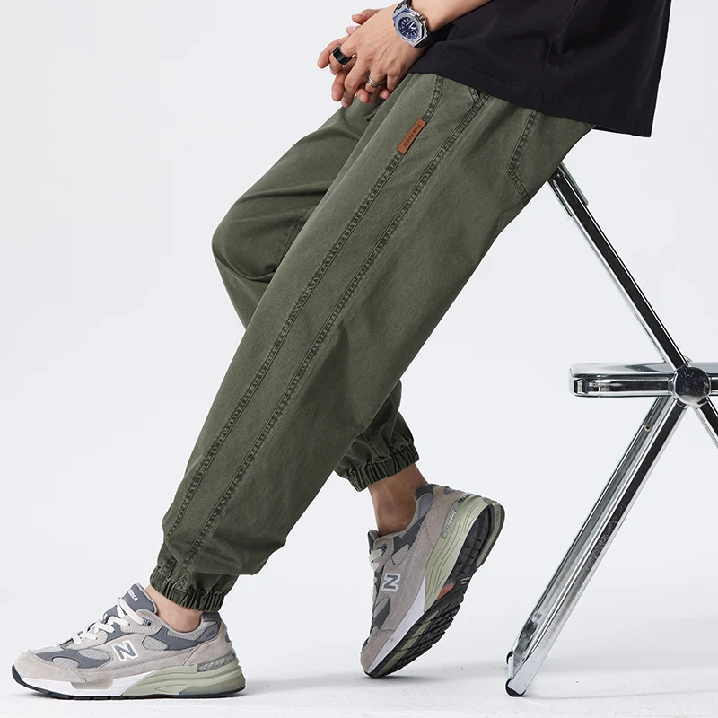 Mann trägt olivgrüne Jogginghose und graue Sneakers, sitzt auf einem Stuhl. Bequeme Freizeitmode, sportlicher Look, Herrenbekleidung.
