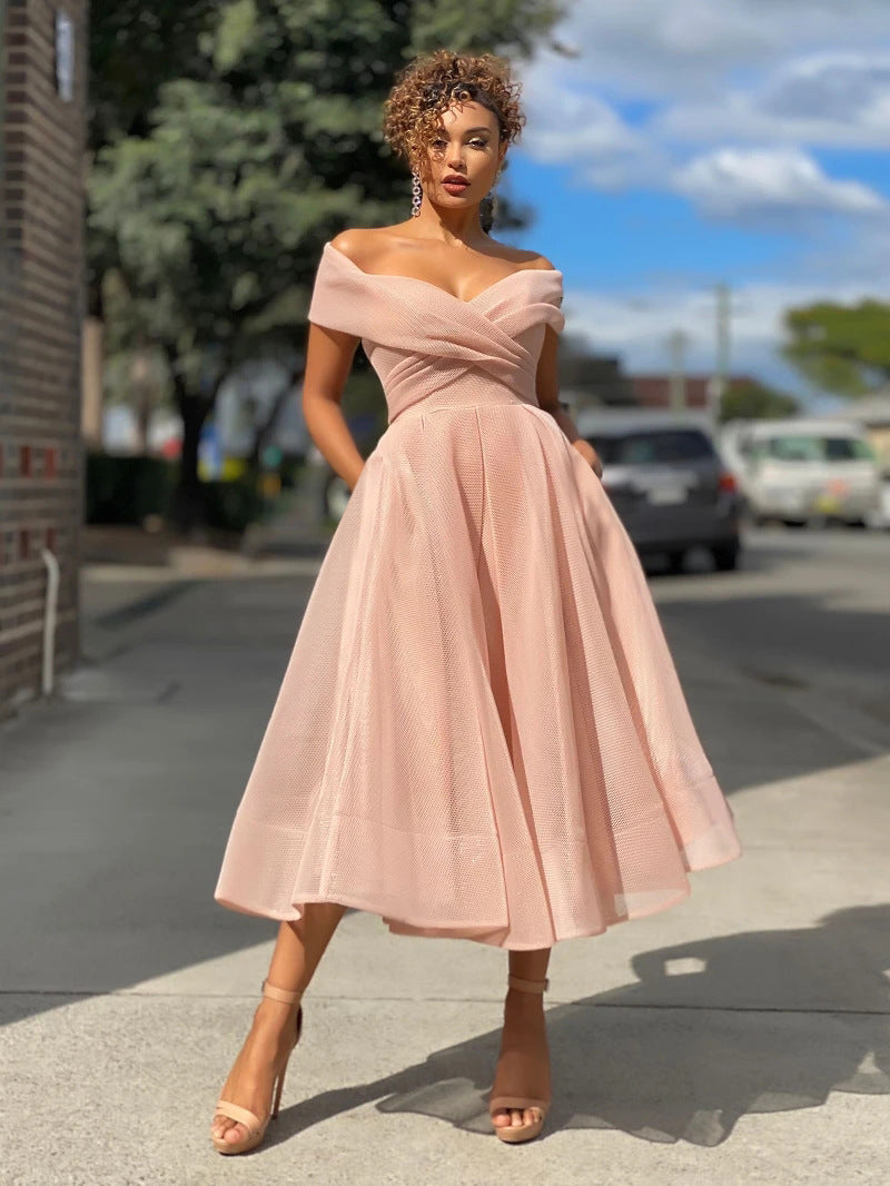 Frau in elegantem, schulterfreiem rosa Kleid auf städtischer Straße, sonniger Tag, modische Abendgarderobe, stilvolle Sandalen, natürliche Locken.
