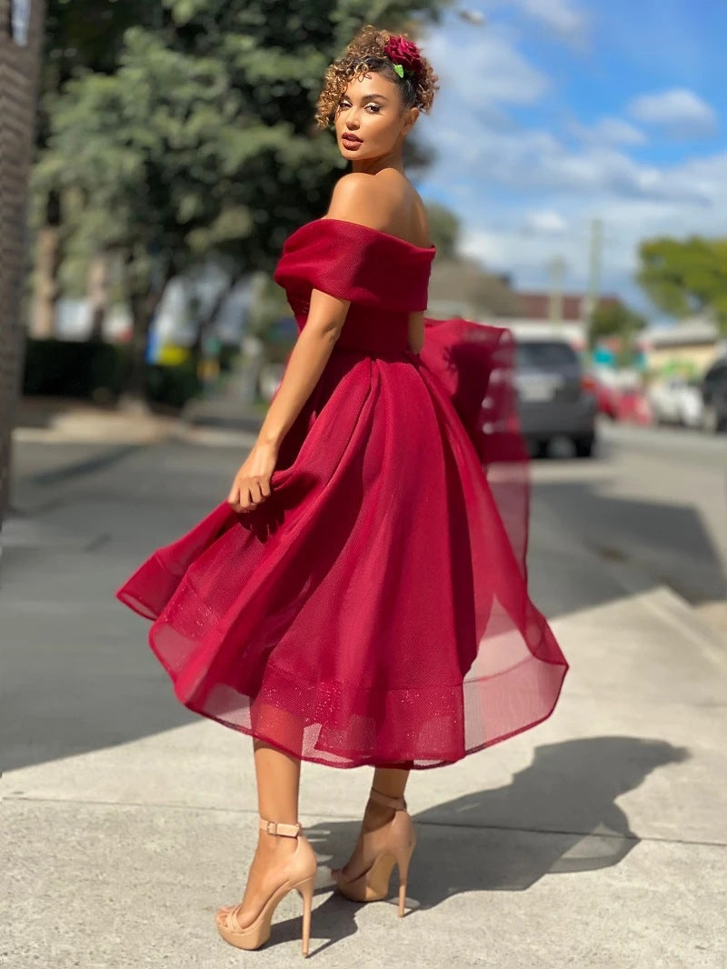 Frau in rotem, schulterfreiem Kleid auf Gehweg, elegantes Abendoutfit, sommerliche Mode, hohe Absätze, stilvolle Frisur, Stadtstraße im Hintergrund.
