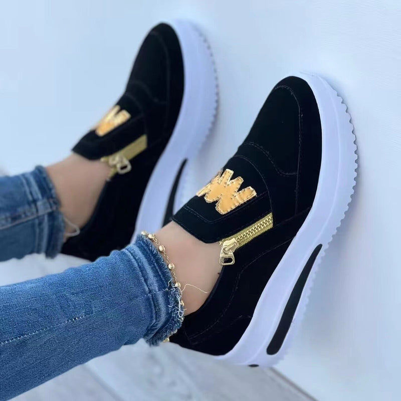 Schwarze Damen-Sneaker mit goldenen Details und Reißverschluss, kombiniert mit blauen Jeans. Modische Freizeitschuhe, ideal für trendbewusste Outfits.