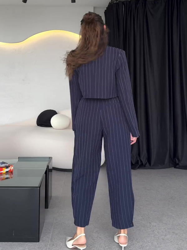 Frau in gestreiftem Anzug von hinten, moderne Inneneinrichtung, schwarze Vorhänge, stilvolle Mode, elegantes Design, zeitgenössischer Look.