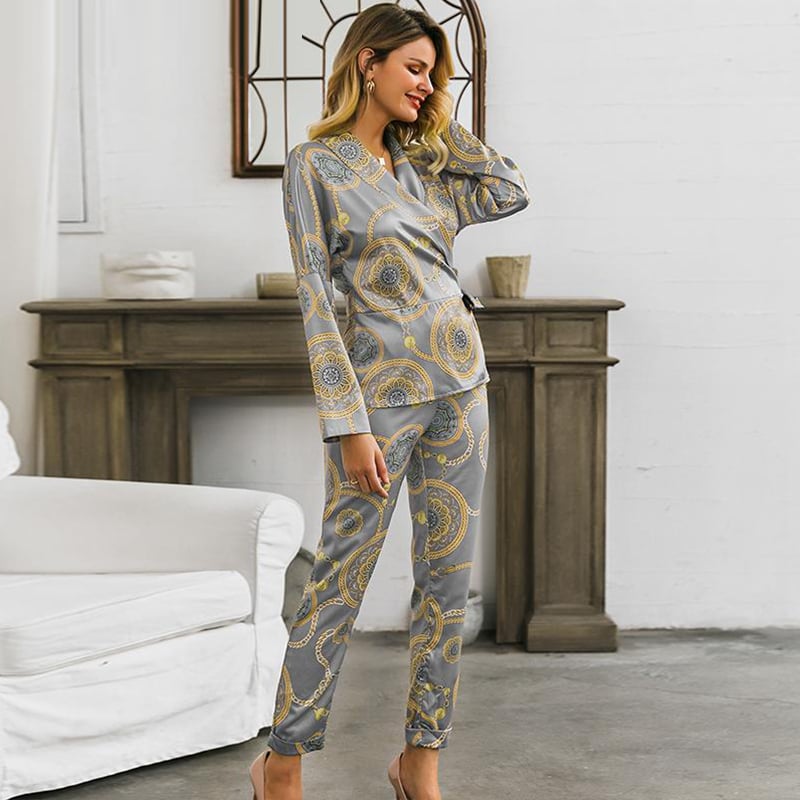 Frau in eleganten, grauen Pyjamas mit goldenen Mustern steht in modernem Wohnzimmer. Bequeme Nachtwäsche, stilvolles Design, gemütliche Atmosphäre.