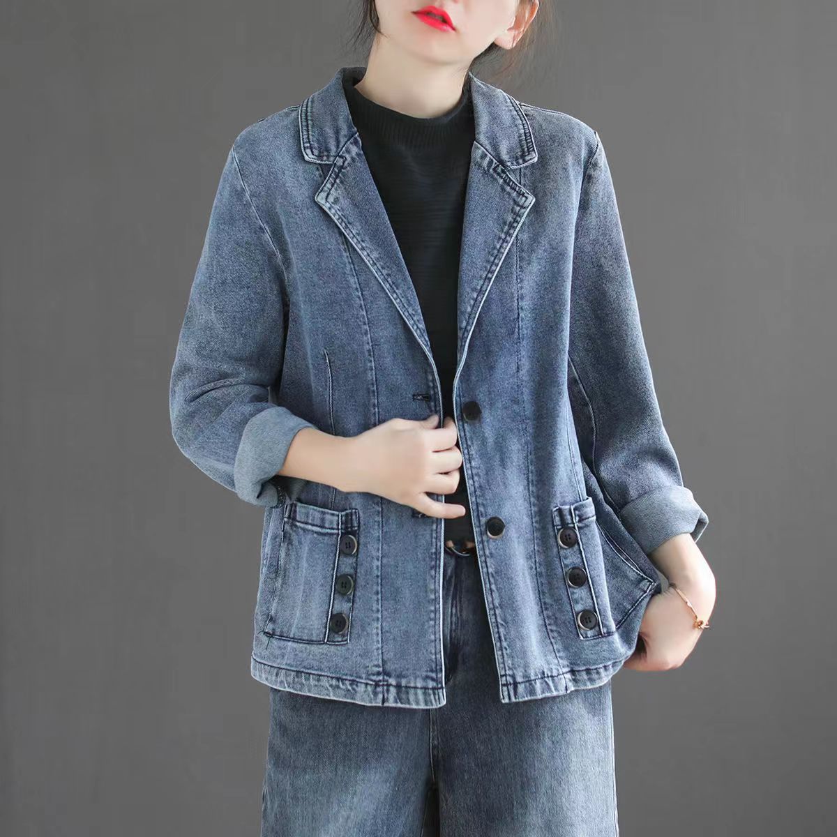 Frau in modischer Jeansjacke mit Knöpfen, kombiniert mit Jeanshose. Trendige Damenmode, lässiger Look, grauer Hintergrund.