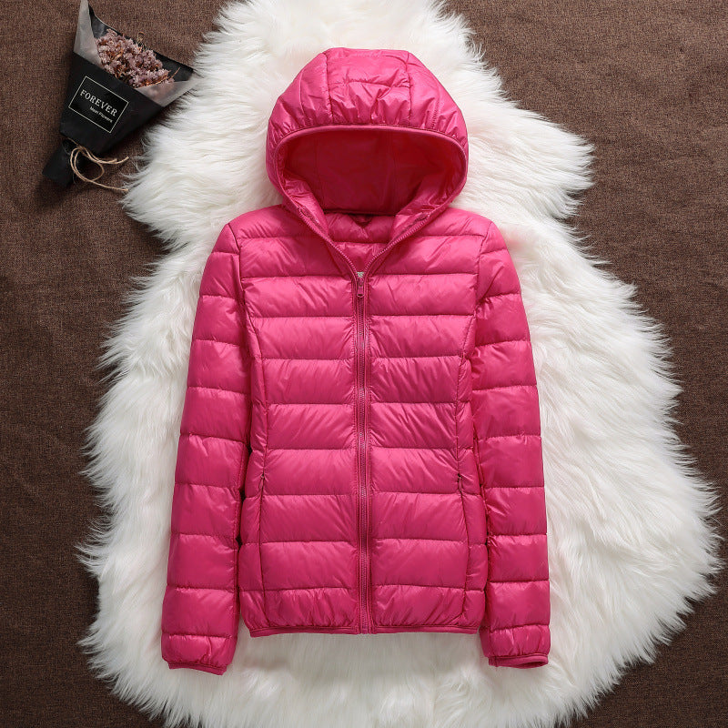 Pinkfarbene Daunenjacke mit Kapuze auf weißem Fellteppich, stilvoll und warm, ideal für Wintermode. Perfekt für Damenbekleidung und Outdoor-Aktivitäten.