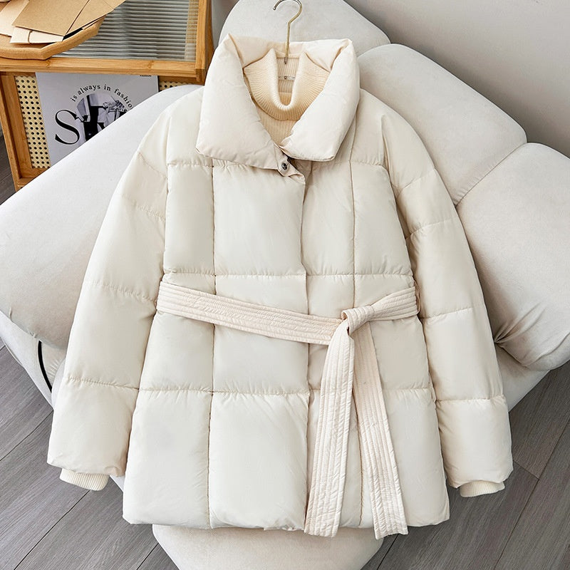 Weiße Daunenjacke mit Gürtel auf Sofa, modisch und warm, ideal für Wintermode. Hochwertige Materialien, stilvolles Design, perfekte Winterbekleidung.